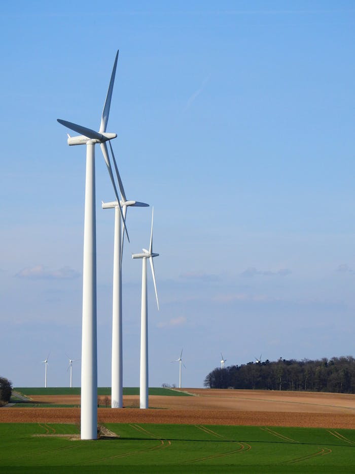 about-img-01 Row of wind turbines in a rural area, generating renewable energy under a blue sky.